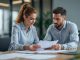 Une femme responsable pédagogique et un homme responsable RH comparent des contrats d’assurance pour étudiants, alternants et apprentis autour d’une table de réunion, avec des documents et un ordinateur portable dans un bureau lumineux.