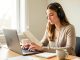 Une jeune femme étudie seule à son bureau, utilise un ordinateur portable, prend des notes dans un carnet et porte un casque audio dans une ambiance lumineuse et calme.