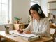 Jeune femme portant un casque audio, prenant des notes à son bureau dans une salle d’étude moderne et lumineuse.