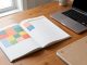 Agenda annuel ouvert sur un bureau en bois, avec des blocs de couleurs représentant les périodes de vacances, un ordinateur portable et un carnet de formation.