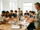 Groupe d’apprentis, hommes et femmes, réalisant une activité collaborative autour d’une table pendant qu’un formateur les observe dans un atelier lumineux et professionnel.