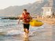 Jeune homme nageur sauveteur courant dans les vagues avec une bouée de sauvetage lors d’un entraînement sur la plage d’Argelès-sur-Mer, avec un poste de secours en arrière-plan.